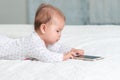 Portrait of baby is lying on the bed and playing with a smartphone. Side view. Copy space. Concept of children`s games with moder Royalty Free Stock Photo