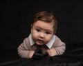 Portrait of a baby lying on his stomach wearing a tie on a black background.