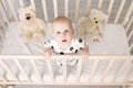 Portrait of a baby 8 months old standing in a crib with toys in pajamas in a bright children`s room after sleeping and looking at Royalty Free Stock Photo