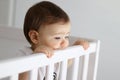 Portrait of baby staying in his baby cot looking sadly