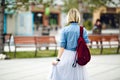 A portrait of the back of a girl holding marsala backpack wearing blue denim shirt and grey tulle skirt. A girl walks in Royalty Free Stock Photo