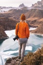 Portrait from the back of the girl traveler photographer in an orange sweater and hat with a camera in hand in the