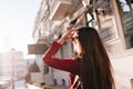 Portrait from back of long-haired girl walking around city in sunny day. Brunette lady in red jacket looking at sky on Royalty Free Stock Photo