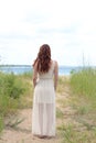 Back of redhead woman with lace dress on beach path