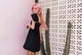 Portrait from back of tanned woman with pink hair smiling beside cactus. Photo of european pleasant