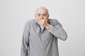 Portrait of bald adult man covering his mouth with hand expressing fear and shock over white background. Guy in casual