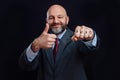 Portrait of a bald business man in suit on dark background. Smile on the face, thumbs up and sign boss on his fist. The model is Royalty Free Stock Photo