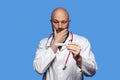 Portrait of bald doctor on blue background. Male health care worker in 40s, with grey beard holding white digital thermometer, Royalty Free Stock Photo