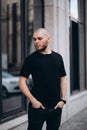 Portrait of a bald handsome bearded man in a black t-shirt on the street, who looks away