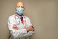 Portrait on a bald male doctor on a light background. Man in his 40s wearing white uniform and blue face mask, red stethoscope and