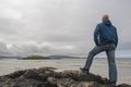 Portrait of bald man standing on a rock by the ocean, hands on his hips, back to camera, beautiful and calm scenery in the Royalty Free Stock Photo