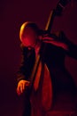 Portrait of bald musician in glasses plays double bass in red-yellow light against gradient studio background. Royalty Free Stock Photo