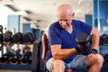 A portrait of senior man in the gym training with dumbbells. People, health and lifestyle concept