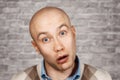 Portrait of a bald stupid surprised guy with open mouth on an brick wall background