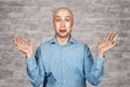 Portrait bald unsure man doesn`t understand anything and spreads his hands. guy in a blue shirt on white brick wall background in