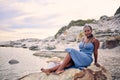 Portrait, beach or black woman on rock to relax on holiday vacation or resting break in Greece at sunset. Tourist, girl