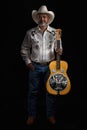 Portrait of bearded Asian musician dons cowboy attire, clutching a Dobro guitar on a black backdrop