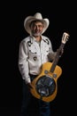 Portrait of bearded Asian musician dons cowboy attire, clutching a Dobro guitar on a black backdrop