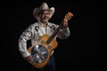 Portrait of bearded Asian musician dons cowboy attire, clutching a Dobro guitar on a black backdrop