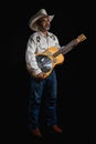 Portrait of bearded Asian musician dons cowboy attire, clutching a Dobro guitar on a black backdrop