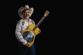 Portrait of bearded Asian musician dons cowboy attire, clutching a Dobro guitar on a black backdrop