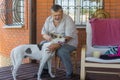 Portrait of bearded Caucasian senior man stroking his white mixed breed dog while sitting on veranda Royalty Free Stock Photo