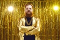 Portrait of man in shiny disco jacket and gold chain necklace standing arms folded