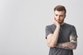 Portrait of bearded handsome man with stylish hairstyle and tattooed arm holding head with hand looking aside with tired Royalty Free Stock Photo