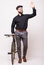 Portrait of a bearded handsome young man walking with fixie bicycle and wave hello gesture over white background