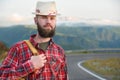 Portrait of a bearded happy smiling traveler hipster with a backpack in a plaid shirt and a hat next to an unknown car