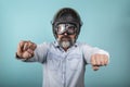 Portrait of bearded hipster in denim shirt with helmet and glasses pretending to ride a motorcycle, isolated on blue studio wall