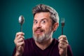 A portrait of bearded man holding spoon and fork in hands. People and food concept