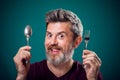 A portrait of bearded man holding spoon and fork in hands. People and food concept