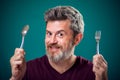 A portrait of bearded man holding spoon and fork in hands. People and food concept