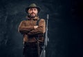 Portrait of a bearded hunter with rifle posing with his arms crossed. Studio photo against a dark wall background