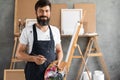 portrait of a bearded male artist in a dirty apron stands in an art studio and looks into the camera. holds in his hands Royalty Free Stock Photo