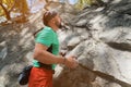 Portrait of a bearded male climber training in the forest stands in front of a rock looks at the rock route