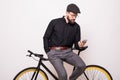 Portrait of a bearded man leaning on fixie bicycle typing on the mobile phone over white background