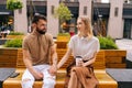 Portrait of bearded man with tattooed hand and blonde young woman having carefree talk sitting on bench holding hands Royalty Free Stock Photo