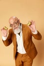 Portrait of bearded, mature, bald businessman in elegant, classical suit posing with golden coins against studio