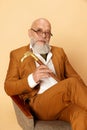 Portrait of bearded, mature, bald man in elegant, classical suit sitting in armchair, looking at camera and smiling