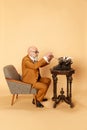 Portrait of bearded, mature, bald man in elegant, classical suit sitting in front of typewriter and working against