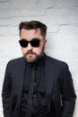 Portrait of a bearded serious man in sunglasses and a business black suit against a white brick wall Royalty Free Stock Photo