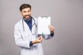 Portrait of bearded smiling intern, who is holding the clipboard with empty paper. Doctor is wearing white uniform, stands over Royalty Free Stock Photo