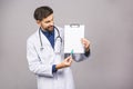 Portrait of bearded smiling intern, who is holding the clipboard with empty paper. Doctor is wearing white uniform, stands over Royalty Free Stock Photo