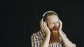 Portrait of bearded young man puts on headphones and dancing while listen to music on black background Royalty Free Stock Photo