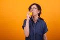 Portrait of beaufitul confused young woman while bitting a fresh orange over yellow background