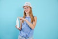 Portrait of beauteous teenage girl with long fair hair holding white sunscreen lotion spray on blue background. Summer.