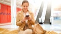 Portrait of beautfiul young woman sitting in shopping mall and using smartphone