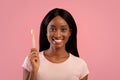 Portrait of beautiful African American woman with radiant smile holding wooden toothbrush with paste on pink background Royalty Free Stock Photo